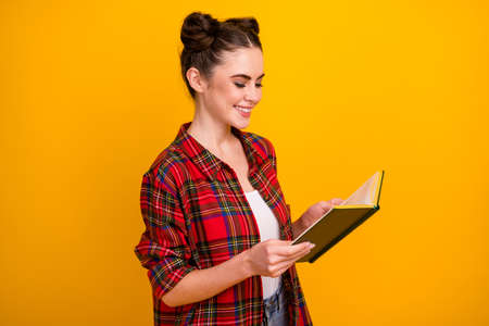 Profile photo of pretty lady two cute buns hold book read interesting love story favorite historic novel wear casual white red plaid shirt isolated yellow color backgroundの写真素材