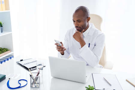 Photo of family doc dark skin guy watch notebook medical news online consultation use telephone read...