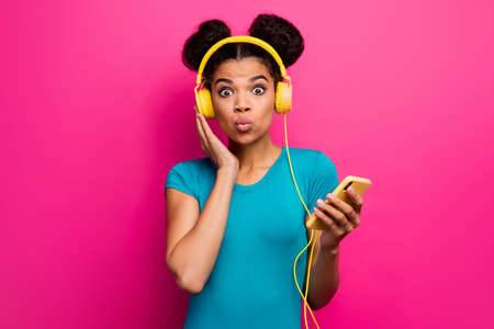 Photo of pretty funky dark skin lady hold telephone listen music modern technology earphones crazy facial expression wear blue casual t-shirt isolated bright pink color backgroundの写真素材
