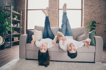 Portrait of nice attractive lovely funny comic cheerful cheery optimistic, friends friendship lying on divan having fun showing v-sign at modern industrial loft style brick interior houseの写真素材