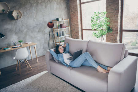 Nice attractive cheerful cheery slim fit thin girl lying on divan using laptop studying watching web tutorial spending free time in modern loft brick industrial house apartmentの写真素材
