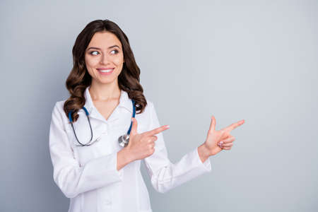 Photo of beautiful doc lady virology clinic direct fingers empty space show pandemic rules disinfection avoiding respiratory symptom wear lab coat stethoscope isolated grey color backgroundの写真素材