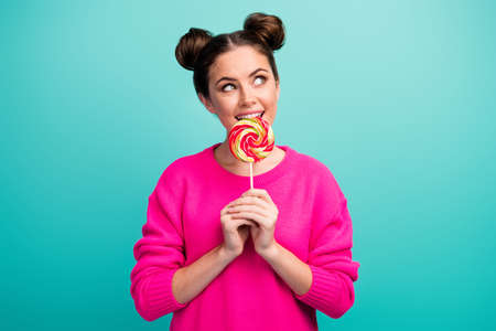 Portrait of attractive lovely childish cheerful cheery wavy-haired girl biting lollipop thinking isolated over bright vivid shine vibrant green blue color backgroundの写真素材