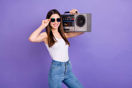 Portrait of positive cheerful youth girl enjoy listen retro music hold shoulders boom box wear sunglass good look outfit isolated over vivid color backgroundの写真素材