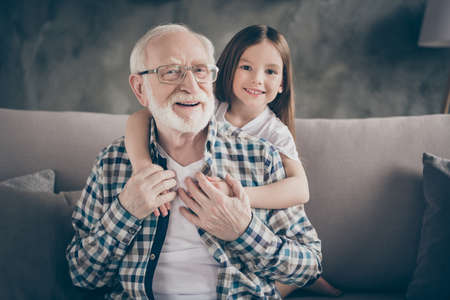 Photo of funny two people old grandpa little granddaughter sitting sofa stay house quarantine safety hugging piggyback modern design interior living room indoorsの写真素材