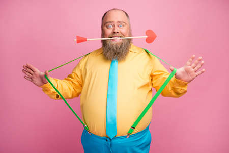 Portrait of his he nice friendly funky glad positive bearded guy holding in teeth mouth amorous arrow pulling suspenders having fun isolated over pink pastel color backgroundの写真素材