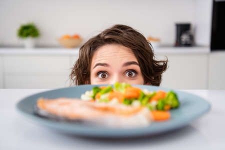 Close up photo of housewife lady cunning tricky hungry eyes look from under table ready to eat grilled salmon trout fillet steak garnish portion modern kitchen indoorsの写真素材
