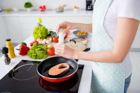 Cropped photo of housewife lady hands put fresh raw salmon fillet steak lying, flying pan adding spices salty cooking family dinner wear apron t-shirt stand modern kitchen indoorsの写真素材