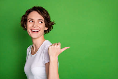 Closeup profile photo of funny attractive lady wavy hairdo direct thumb finger side empty space offer cool sale shopping prices wear casual white t-shirt isolated green color backgroundの写真素材