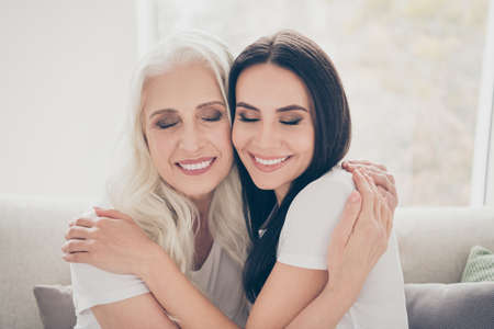 Close-up portrait of two nice attractive lovely cheerful dreamy women mom daughter granny granddaughter hugging enjoying holiday daydream in house apartment indoorsの写真素材