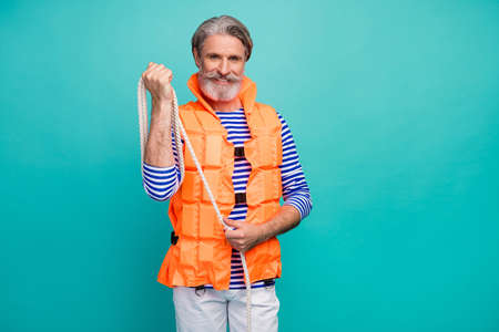 Photo of attractive strong aged seaman wounding rope around hand lifeguard cruise ship boat wear striped sailor shirt orange life vest isolated teal color backgroundの写真素材