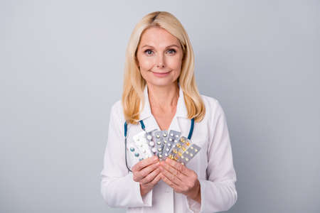 Positive doctor woman hold pills effective corona virus antidote wear stethoscope white coat isolated over gray color backgroundの写真素材
