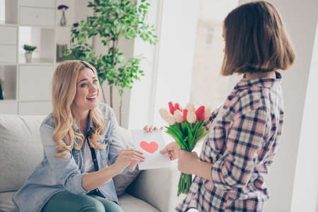 Positive mommy sit cozy couch get receive present bloom blossom bunch tulips postcard from her daughter in house indoorsの写真素材