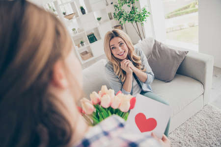 Oh dear its for me. Low angle view photo adorable mature woman sit comfort couch impressed schoolgirl give blossom bunch tulips postcard 8-march two people in house indoorsの写真素材