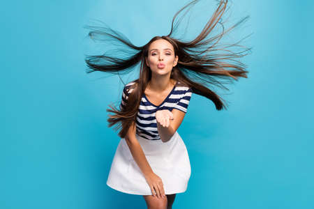 Photo of funny lovely lady enjoy summer breeze long hairdo flight relaxing weather send air kisses boyfriend wear white striped sun mini summer dress isolated blue backgroundの写真素材