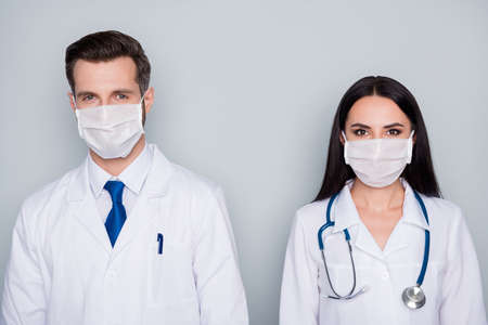 Photo of professional doc guy lady virology clinic avoid contacting patients stand distance experienced doctors wear protective facial masks lab coats isolated grey color backgroundの写真素材