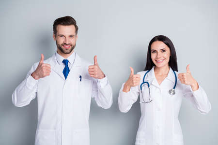 Photo of handsome doc guy lady two people emergency patient consultation virology clinic thumbs up approve health condition experienced doctors wear lab coats isolated grey color backgroundの写真素材