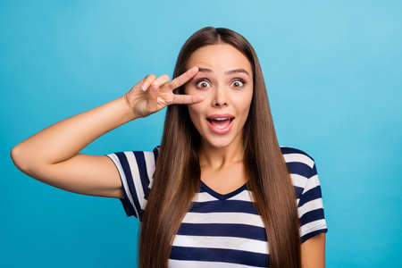 Closeup photo of pretty beautiful lady long hairdo showing two fingers v-sign near eye good mood open mouth excited wear white striped sailor t-shirt isolated blue backgroundの写真素材