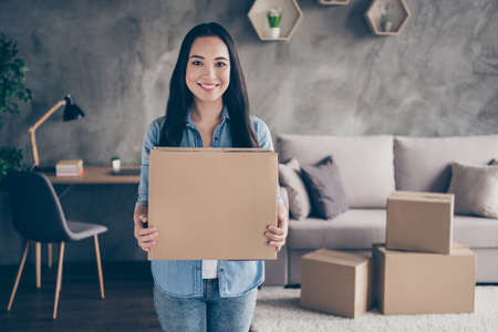 Portrait of charming positive girl hold card board box with her belongings she ready change place of living wear casual style clothes in house indoorsの写真素材
