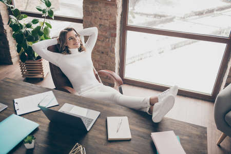 Portrait of her she nice attractive lovely pretty cheerful wavy-haired girl hr recruiter director sitting in chair resting leg on desk modern loft brick industrial interior style workplace workstationの写真素材