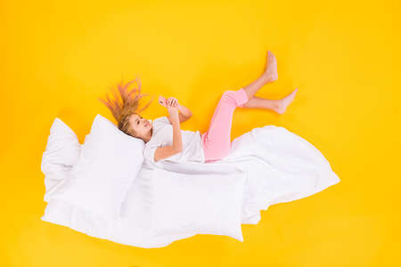Top view above high angle flat lay flatlay lie concept of her she nice cheerful focused girl lying on blanket using cell chatting isolated bright vivid shine vibrant yellow color backgroundの写真素材