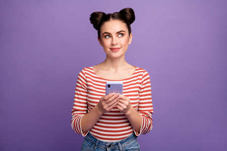 Photo of funny pretty lady hold telephone hands blogger look dreamy up empty space wait inspiration wear white red casual striped shirt isolated purple pastel color backgroundの写真素材