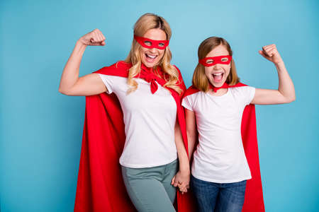 Photo of beautiful mom lady little daughter spend time together carnival super hero costumes showing strength muscles wear s-shirts red coat masks isolated blue color backgroundの写真素材
