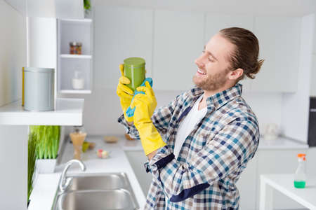 Profile side view portrait of his he nice attractive cheerful cheery guy husband cleansing things furniture washing cleaning service in modern light white interior style kitchenの写真素材