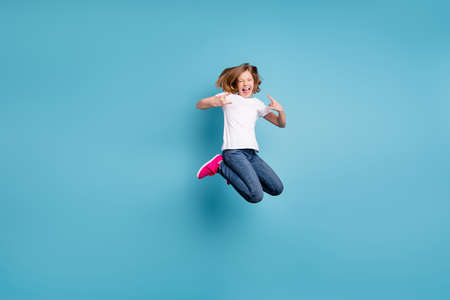 Full length photo of funny little daughter lady spend time jumping high up hold hands horns rejoicing rock concert wear casual white s-shirt jeans isolated blue color backgroundの写真素材