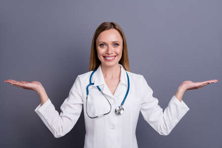 Portrait of her she nice attractive cheerful cheery friendly blonde girl doc therapist holding on two palms copy space advice balance isolated over grey violet pastel color backgroundの写真素材