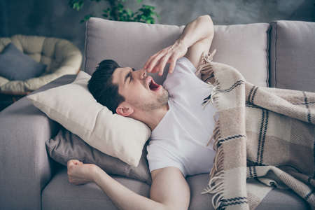 Portrait of his he nice attractive tired sleepy guy lying on divan waking up, resting yawning healthy regime at modern industrial loft brick interior style living-room indoorsの写真素材