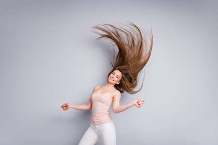 Photo of attractive cute model lady demonstrating ideal neat long healthy hairstyle flying on air after salon procedure wear beige singlet pants isolated grey color backgroundの写真素材