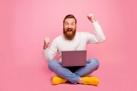 Full length photo excited delighted guy sit floor legs crossed folded work computer celebrate online...