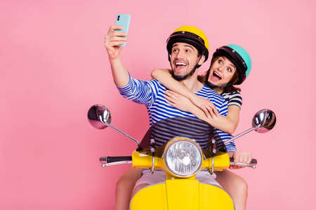 Portrait of his he her she nice attractive cheerful cheery childish funny glad couple driving moped taking making selfie having fun vacation day dream isolated on pink pastel color backgroundの写真素材