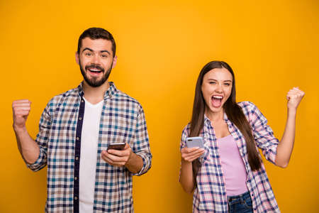 Photo funky lady handsome guy couple rejoicing astonished hold telephones read good news addicted popular bloggers wear casual plaid shirts outfit isolated yellow color backgroundの写真素材