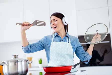 Portrait of funky funny house wife woman cooking supper meal frying pan listen music headset imagine she famous pop star sing spatula in house kitchen indoorsの写真素材