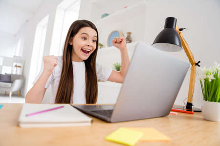 Photo of small pretty overjoyed pupil school girl notebook online lesson video call listen good news nice semester grades best student distance quarantine study comfort room indoorsの写真素材