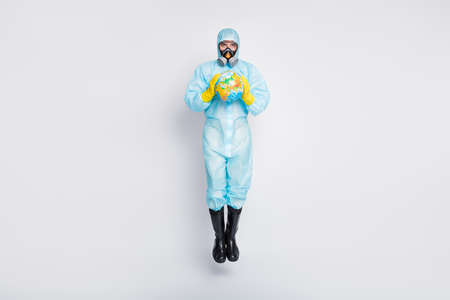 Full length photo clean hygiene man jump hold globe stop international ncov epidemic outbreak wear white suit hazmat yellow rubber latex gloves glasses goggles isolated gray color backgroundの写真素材