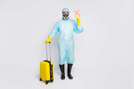 Full length photo man hold bag plane no relax covid quarantine wear white suit biohazard yellow rubber gloves glasses goggles breathing mask isolated gray backgroundの写真素材
