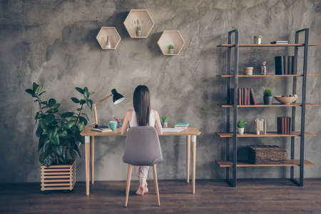 Back rear spine full length photo of concentrated college student girl have, quarantine remote study sit desk prepare home work report in house indoorsの写真素材