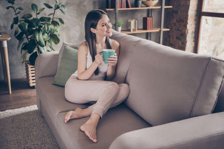 Full size photo of candid content girl sit divan have holiday hold cup coffee look dream future life weekend plan in house indoors apartmentの写真素材