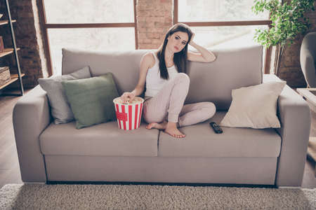 Full length photo of frustrated bored girl sit divan watch uninteresting movie have pop corn box eat stay home in house indoorsの写真素材