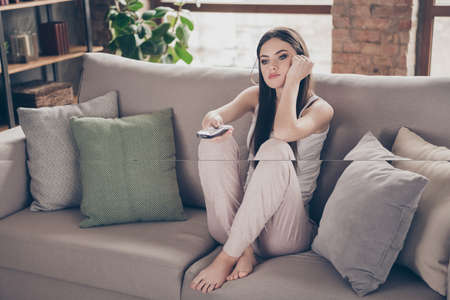 Full length photo of frustrated disappointed girl sit comfy divan watch video uninteresting film use remote control in house indoorsの写真素材