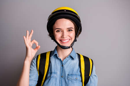 Portrait of positive cheerful girl courier approve covid-29 quarantine delivery food service show okay sign carry yellow thermo bag wear denim jeans shirt isolated silver color backgroundの写真素材