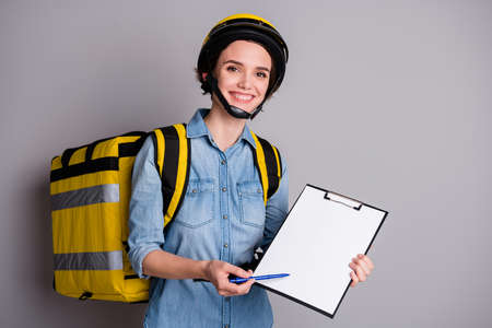 Portrait positive girl courier hold clip board deliver sushi snack lunch ask client put signature white paper carry thermal backpack wear denim jeans shirt isolated gray color backgroundの写真素材