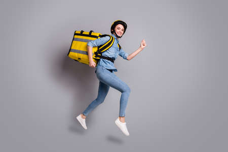 Full body photo positive girl courier jump run want fast deliver meal lunch carry thermal container wear denim jeans shirt helmet isolated gray color backgroundの写真素材