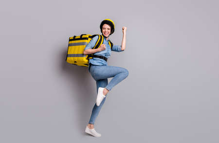 Full body photo crazy ecstatic girl courier deliver  carry thermo container package wear denim jeans shirt helmet isolated gray color backgroundの写真素材