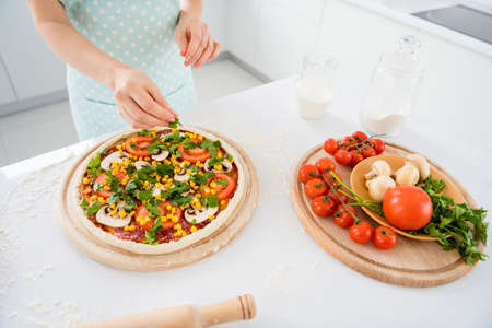 Top above high angle view cropped photo of woman cook delicious pizza with mushroom tomato parsley dressing corn on chopping board in modern kitchen houseの写真素材
