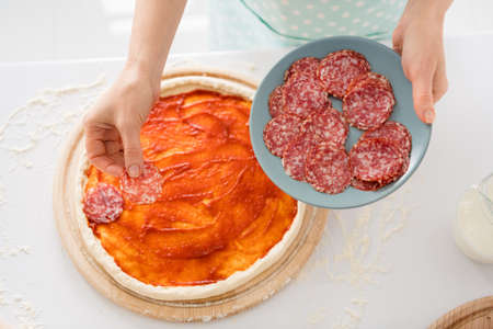 Cropped photo of housewife hands cooking family recipe dinner covering dough pizza ingredients fresh slices sausage standing modern kitchen indoorsの写真素材