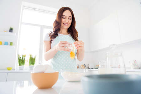 Photo of beautiful housewife early morning weekend preparing cookies for family children husband breaking eggs making dough modern kitchen indoors casual clothingの写真素材